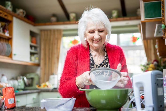 Joyful senior woman sifting flour in a bright kitchen, enjoying an afternoon of baking.
