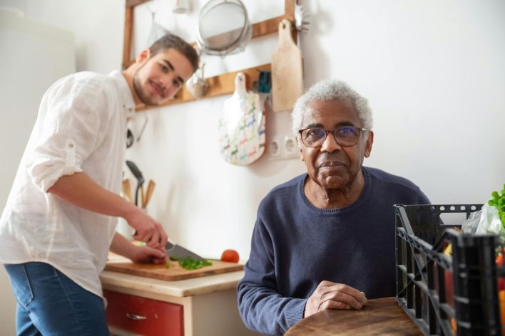 A young adult helping a senior in the kitchen, highlighting care and support at home.