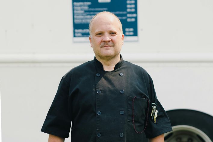 Portrait of a professional chef standing confidently in front of a food truck, wearing a black uniform.
