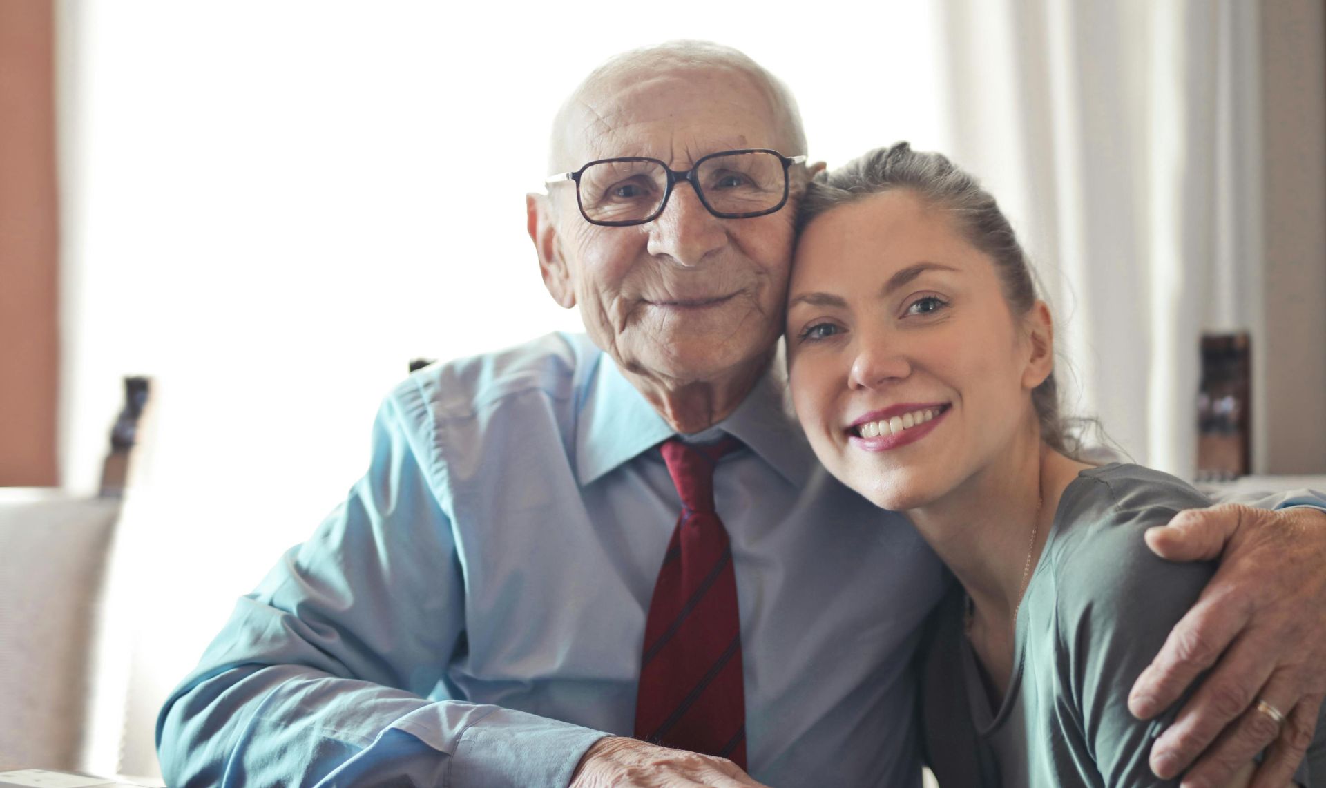 A joyful elderly man and young woman sharing an affectionate embrace indoors.