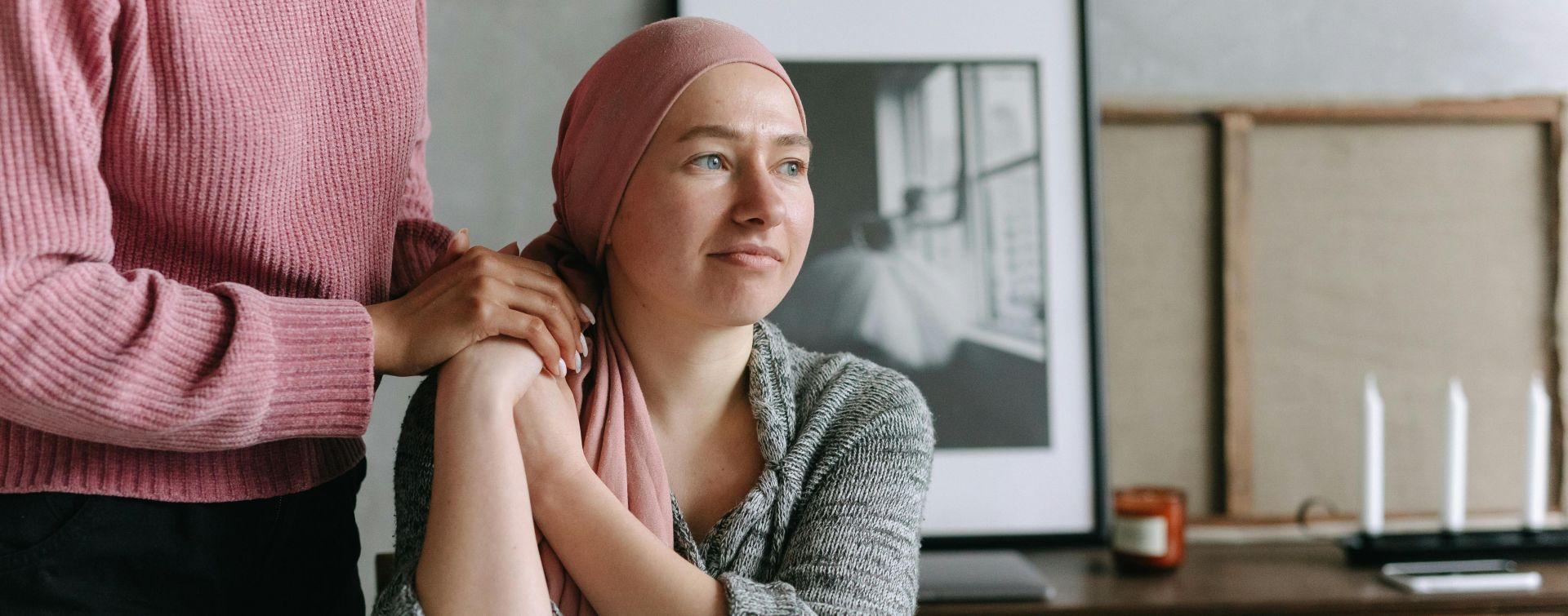 A supportive moment indoors featuring a cancer patient comforted by a friend, conveying emotion and care.
