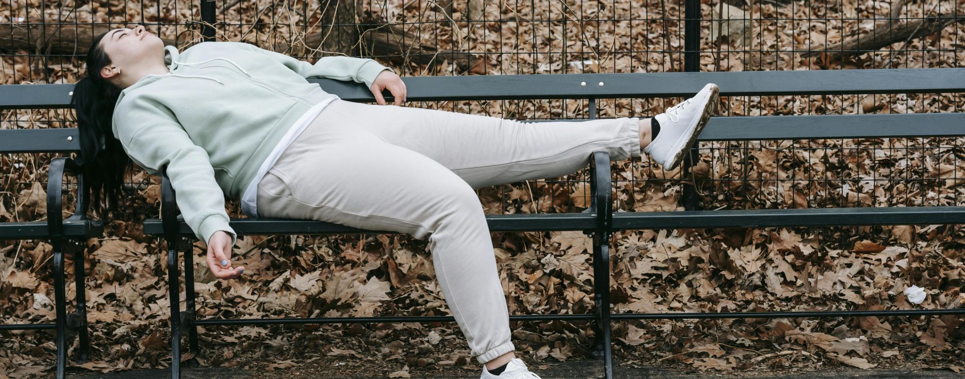 A woman rests on a park bench surrounded by autumn leaves, conveying exhaustion and contemplation.