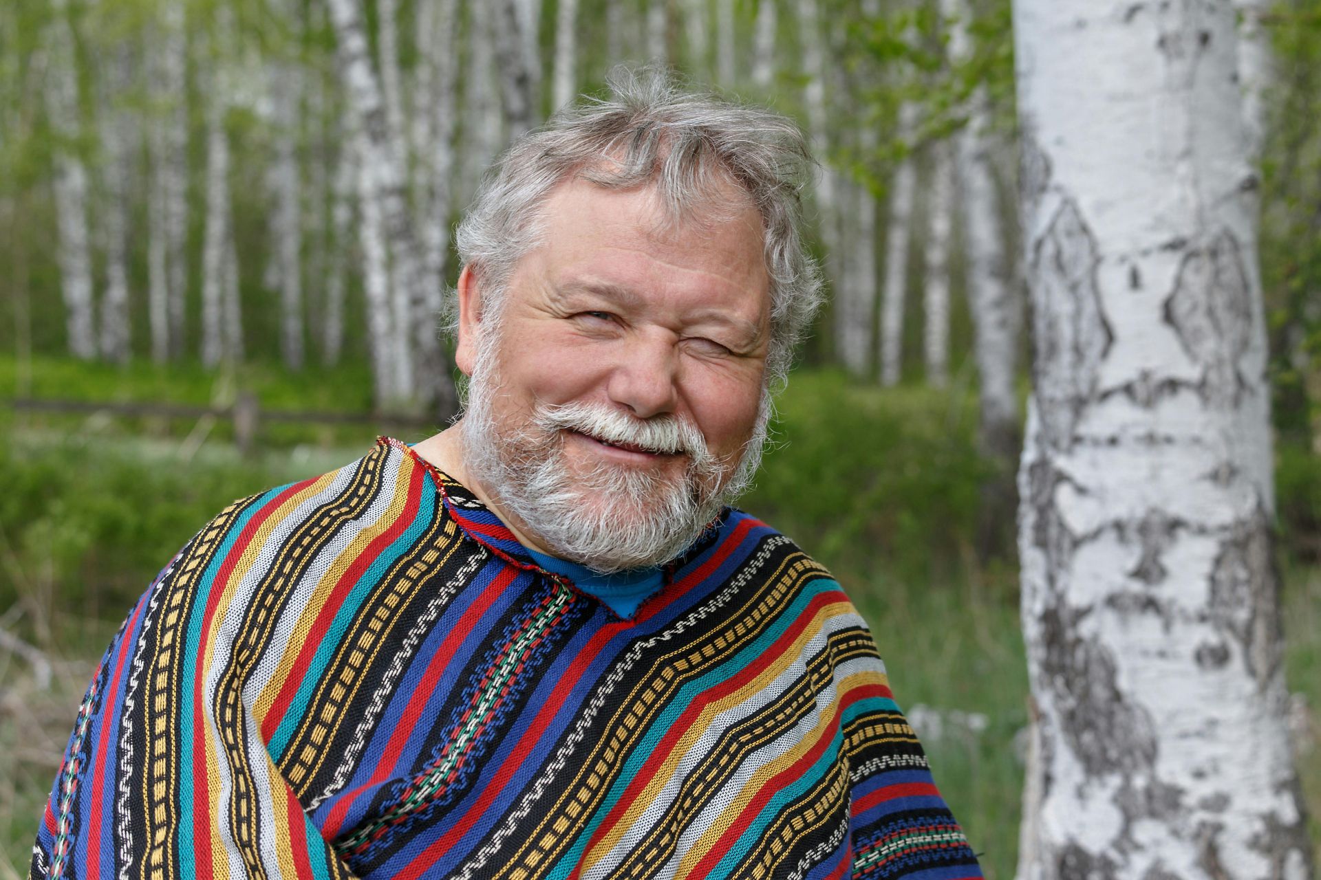A cheerful senior adult man in a colorful poncho happy amidst birch trees since finding the Pop In Concierge Service